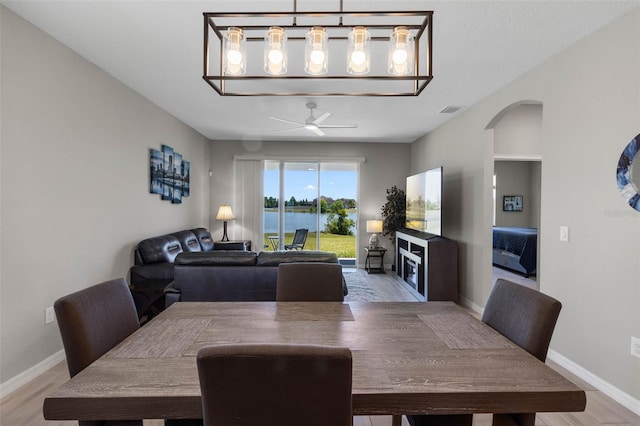 dining area featuring arched walkways, a ceiling fan, baseboards, light wood-type flooring, and visible vents