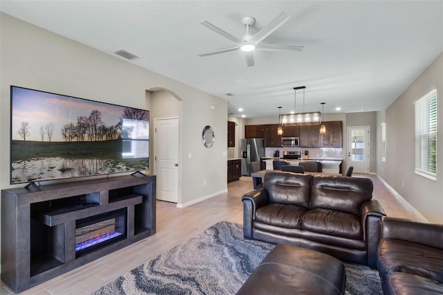 living area with visible vents, baseboards, arched walkways, a ceiling fan, and light wood finished floors