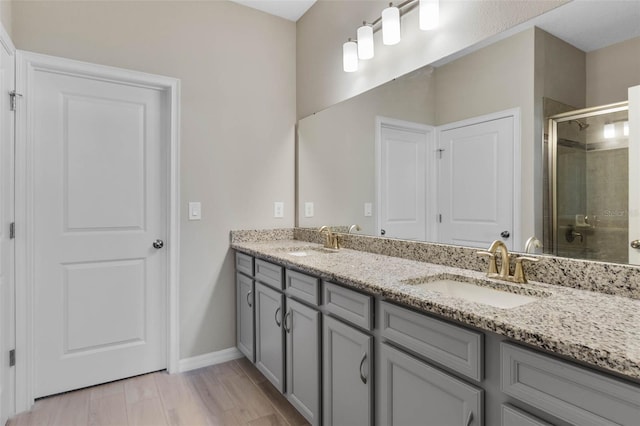 full bath featuring a sink, baseboards, a shower stall, and double vanity