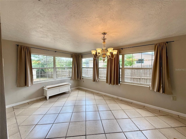 unfurnished room with light tile patterned floors, a textured ceiling, an inviting chandelier, and baseboards
