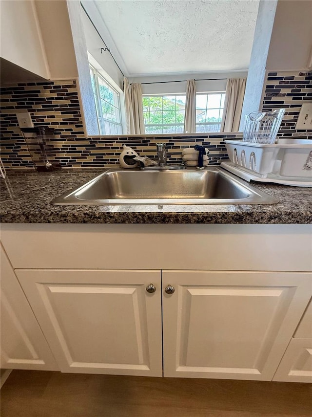 room details featuring dark countertops, a sink, white cabinetry, and tasteful backsplash