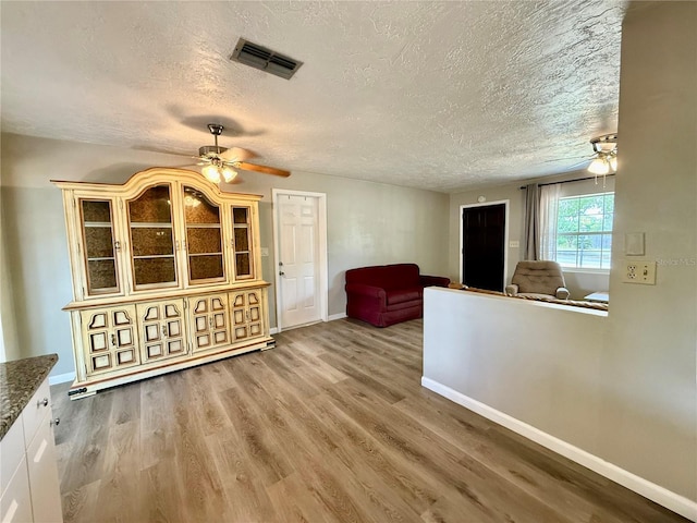 interior space featuring light wood-style floors, visible vents, a ceiling fan, and a textured ceiling