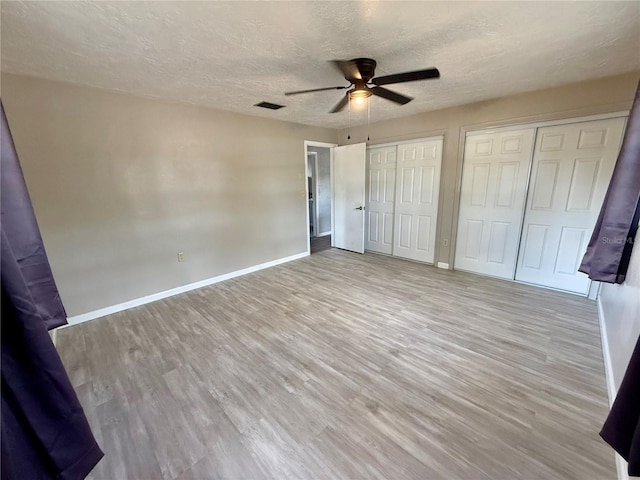 unfurnished bedroom with light wood-style floors, two closets, a ceiling fan, baseboards, and a textured ceiling
