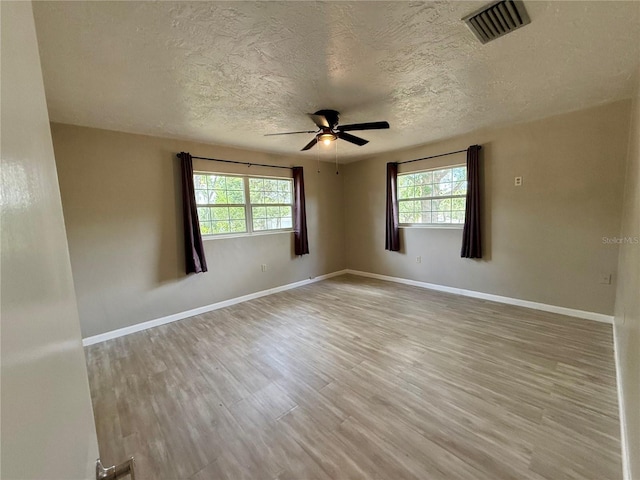 unfurnished room with a textured ceiling, a healthy amount of sunlight, a ceiling fan, and visible vents
