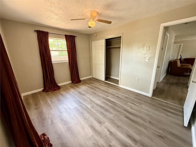 unfurnished bedroom featuring a textured ceiling, baseboards, a closet, wood finished floors, and a ceiling fan