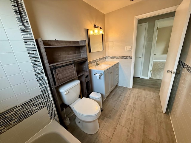 full bathroom featuring tile walls, vanity, toilet, wainscoting, and wood finished floors