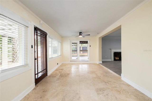 empty room with a fireplace, ceiling fan, ornamental molding, and baseboards