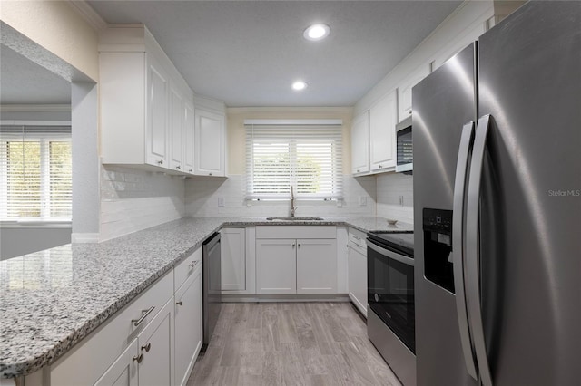 kitchen featuring crown molding, white cabinets, a sink, stainless steel appliances, and light wood finished floors