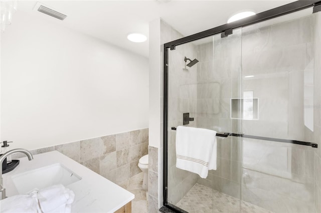 bathroom with visible vents, vanity, wainscoting, tile walls, and a stall shower