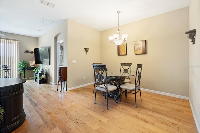dining space featuring visible vents, baseboards, a chandelier, arched walkways, and light wood-style flooring