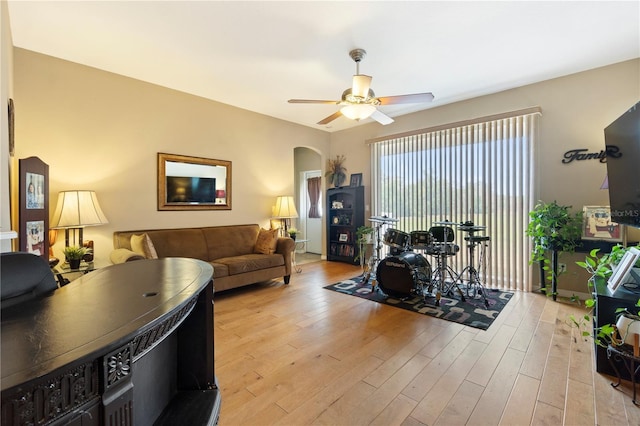 living area with light wood-style floors, arched walkways, and ceiling fan