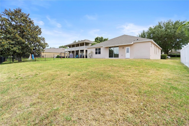 back of house with fence, stucco siding, a yard, and a shingled roof