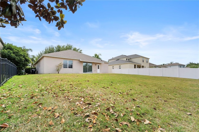 rear view of property featuring a lawn, fence, and stucco siding