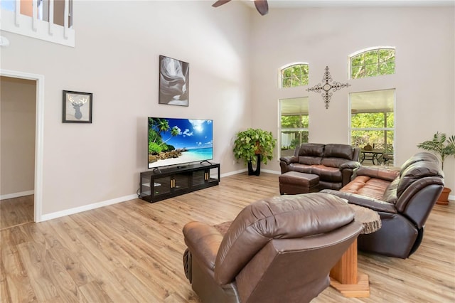 living room with baseboards, a ceiling fan, light wood finished floors, and a high ceiling