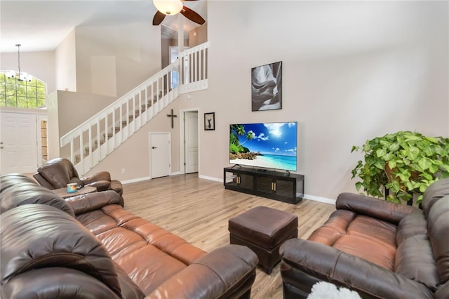living area featuring wood finished floors, stairway, high vaulted ceiling, baseboards, and ceiling fan with notable chandelier
