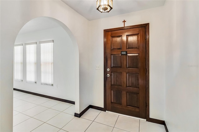 entryway featuring arched walkways, baseboards, and light tile patterned flooring