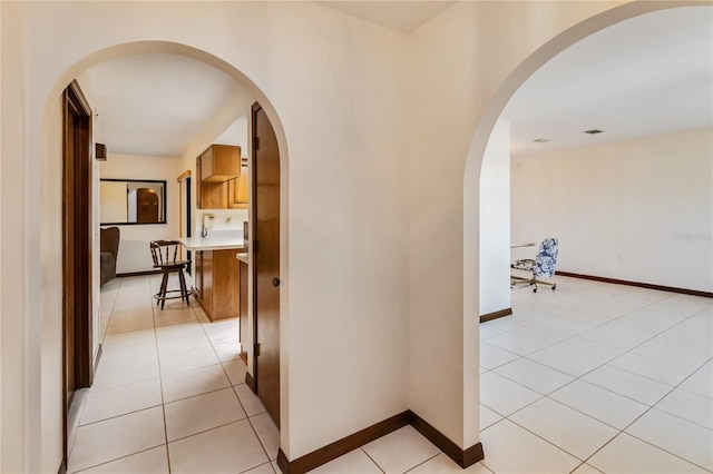 corridor featuring light tile patterned floors, baseboards, and arched walkways