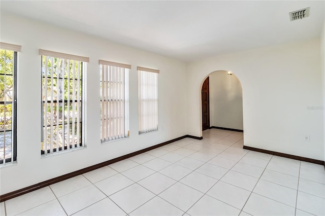 spare room featuring arched walkways, baseboards, and visible vents
