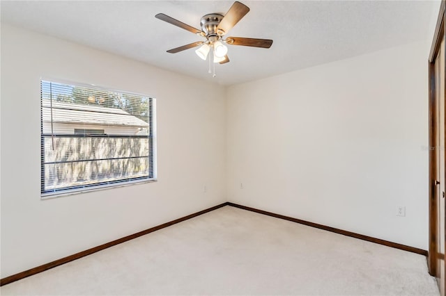 spare room with light colored carpet, baseboards, and ceiling fan