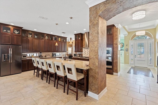 11502 Waterstone Loop Dr, Windermere, FL 34786 - kitchen featuring appliances with stainless steel finishes, a sink, wall chimney range hood, a kitchen breakfast bar, and ornamental molding