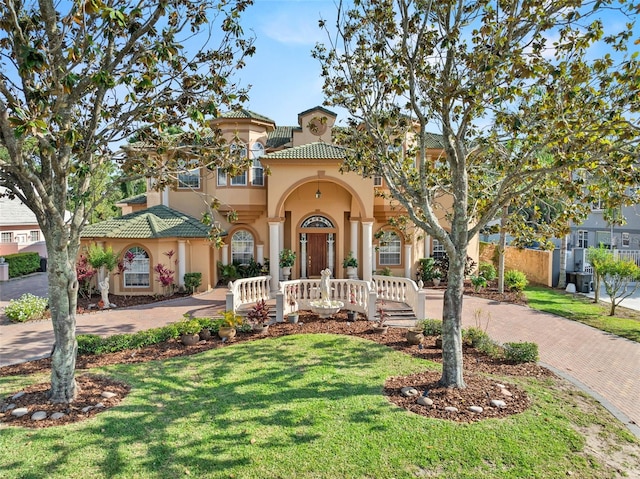 mediterranean / spanish-style home with stucco siding, a front lawn, a tile roof, and decorative driveway