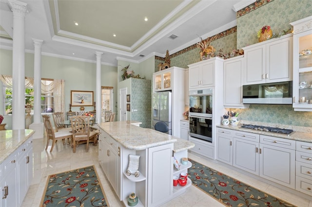 kitchen featuring a raised ceiling, a center island, stainless steel gas stovetop, ornate columns, and multiple ovens
