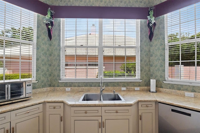 kitchen featuring dishwashing machine, light countertops, a sink, and white cabinetry