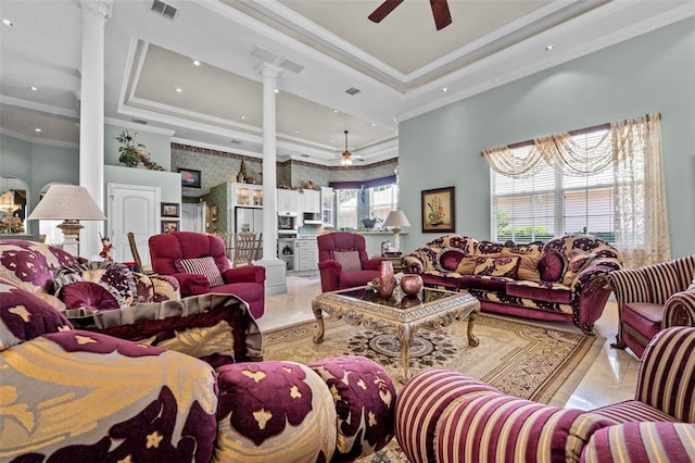 living area featuring a ceiling fan, decorative columns, a tray ceiling, and ornamental molding