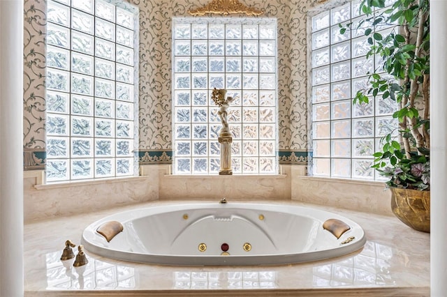 bathroom with a tub with jets, wallpapered walls, and a wealth of natural light