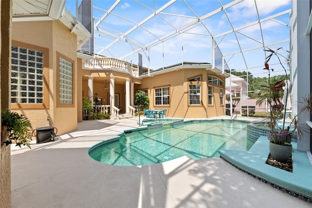 view of swimming pool featuring glass enclosure, a pool with connected hot tub, and a patio area