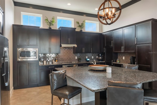 kitchen with a breakfast bar, an inviting chandelier, built in appliances, backsplash, and under cabinet range hood