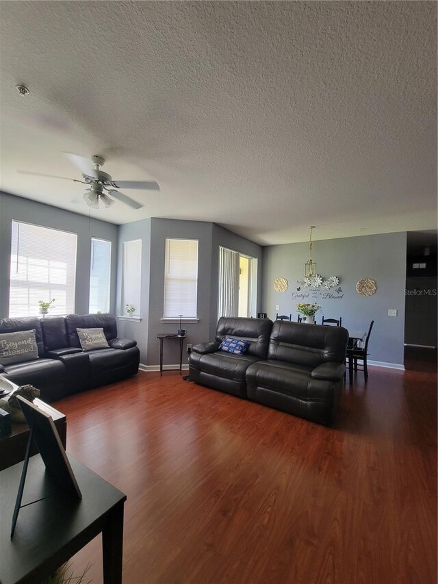 living room featuring baseboards, a textured ceiling, dark wood finished floors, and ceiling fan with notable chandelier