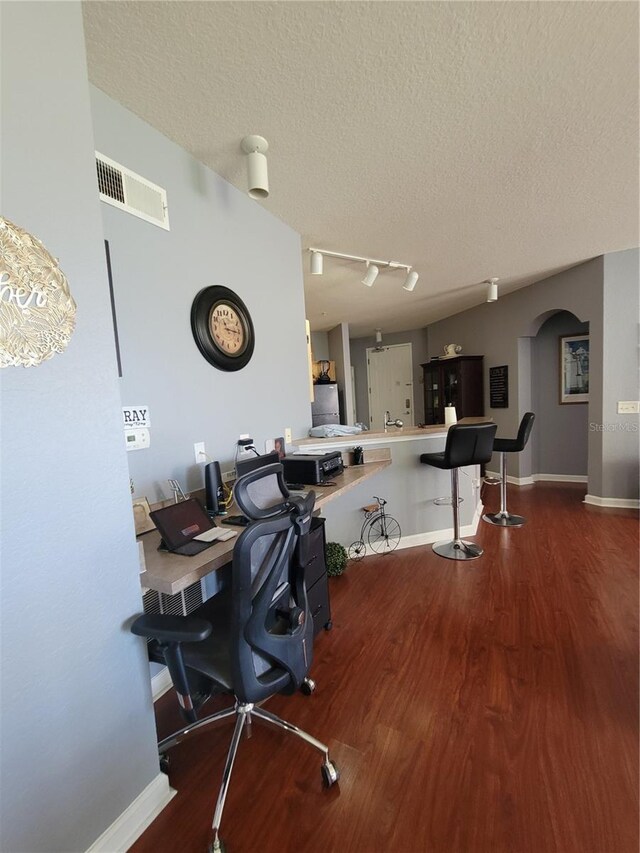 office area with visible vents, track lighting, wood finished floors, a textured ceiling, and arched walkways