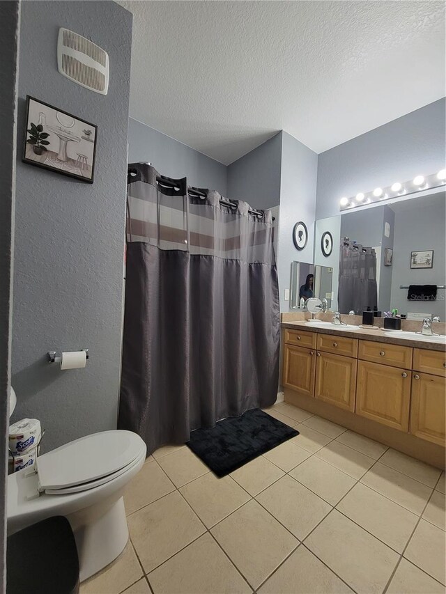 full bath featuring double vanity, a textured ceiling, tile patterned floors, and toilet