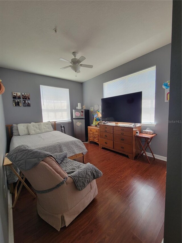 bedroom with baseboards, ceiling fan, freestanding refrigerator, and dark wood-type flooring