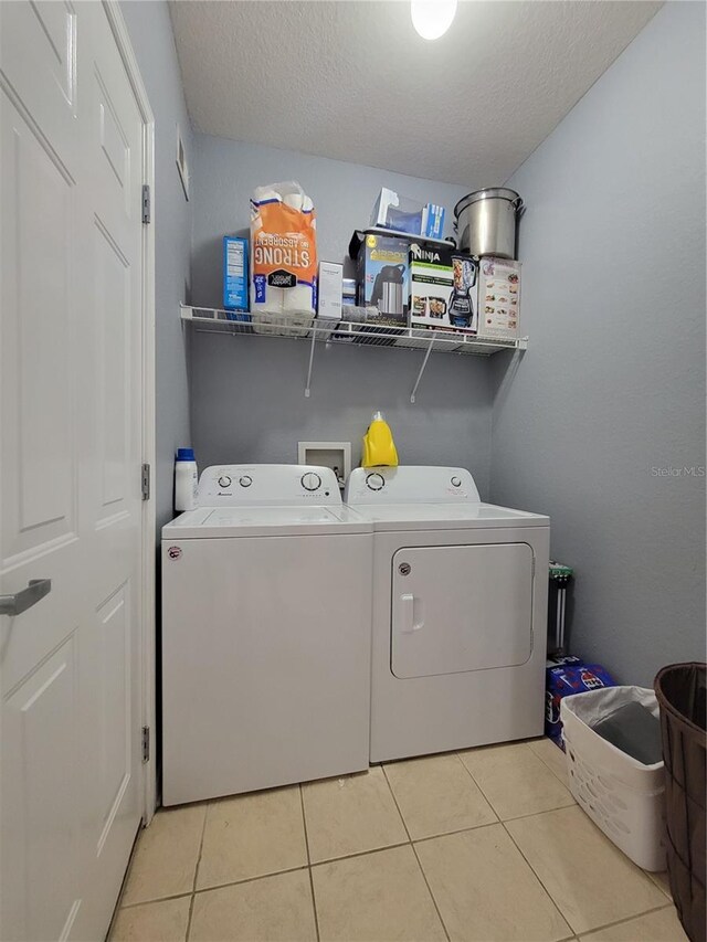 clothes washing area featuring separate washer and dryer, laundry area, a textured ceiling, and light tile patterned flooring