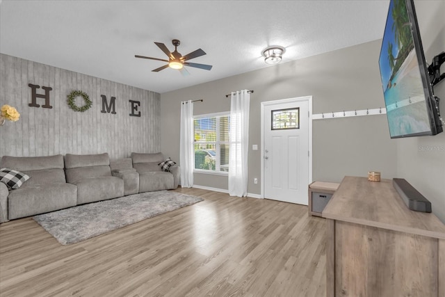 living area featuring baseboards, ceiling fan, an accent wall, and wood finished floors