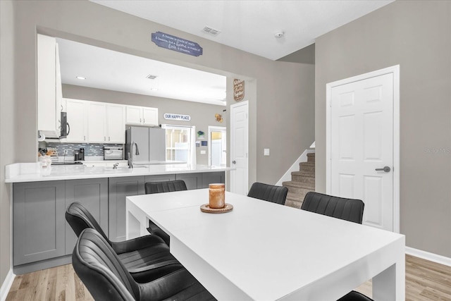 dining space with light wood-style floors, baseboards, stairs, and visible vents