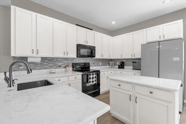 kitchen with light stone counters, a sink, light wood finished floors, decorative backsplash, and black appliances