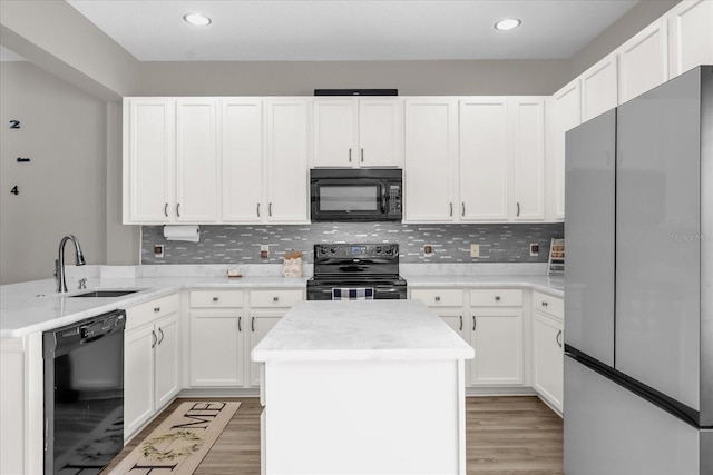 kitchen with a peninsula, a sink, black appliances, and light wood-type flooring