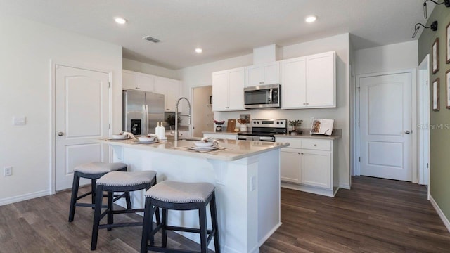 8375 Madrid St, Lakeland, FL 33810 - kitchen featuring dark wood-style flooring, stainless steel appliances, a breakfast bar area, white cabinetry, and an island with sink