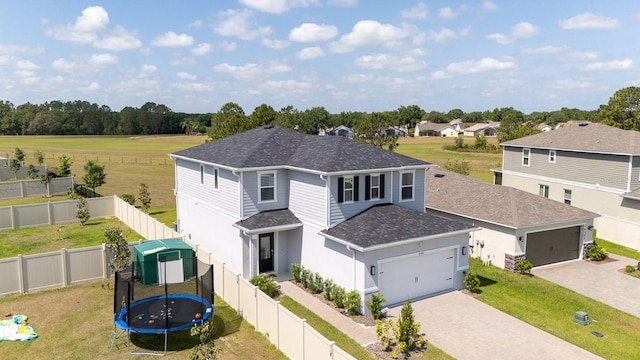 view of front of property featuring a trampoline, roof with shingles, a garage, decorative driveway, and a front lawn
