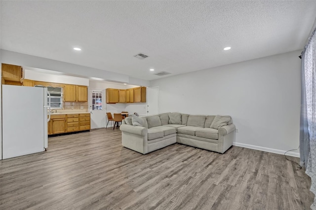 living area featuring a textured ceiling, recessed lighting, light wood-style flooring, and visible vents