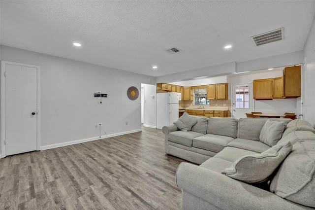 living room featuring recessed lighting, a textured ceiling, visible vents, and light wood-type flooring