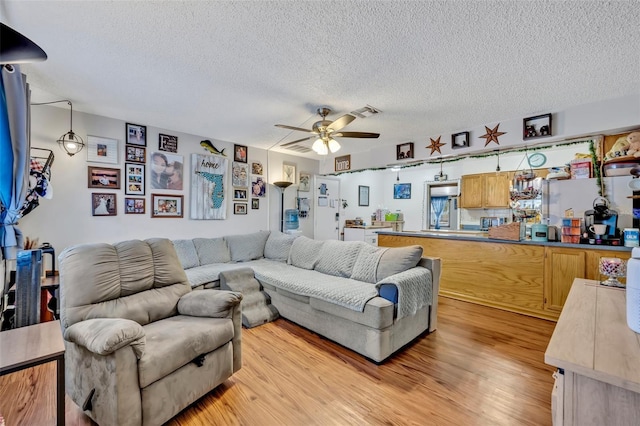 living room featuring ceiling fan, light wood-style flooring, a textured ceiling, and visible vents