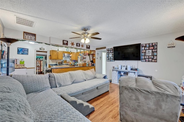 living room with ceiling fan, light wood finished floors, a textured ceiling, and visible vents