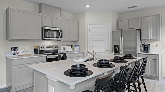 kitchen with gray cabinetry, a breakfast bar, a sink, and appliances with stainless steel finishes