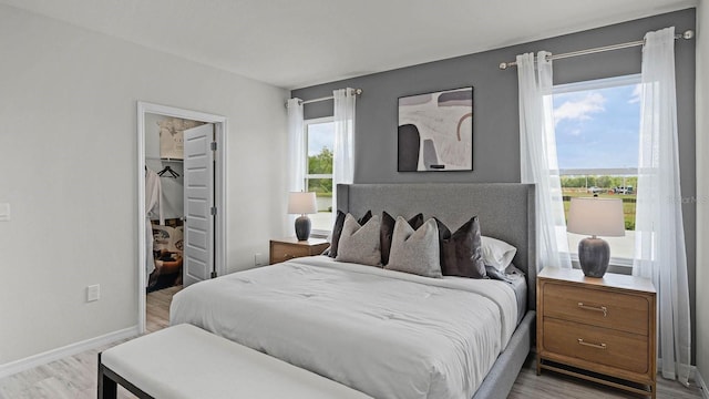 bedroom with a closet, baseboards, light wood-style floors, and a spacious closet