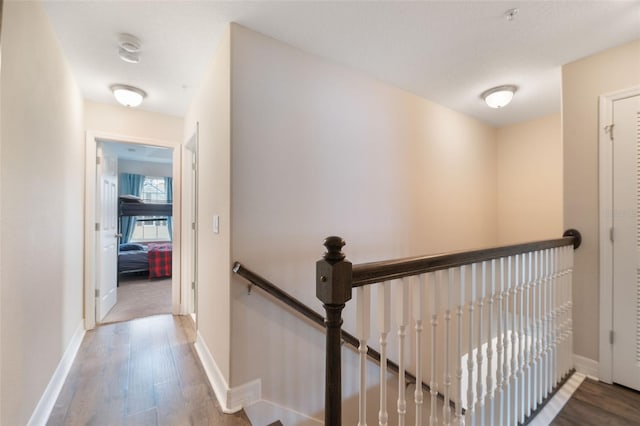 hallway featuring baseboards, an upstairs landing, and wood finished floors