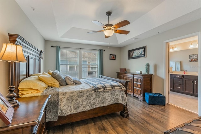 bedroom featuring ensuite bathroom, a ceiling fan, wood finished floors, and a tray ceiling